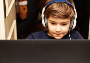 Kid with headphones using computer while e-learning from home.